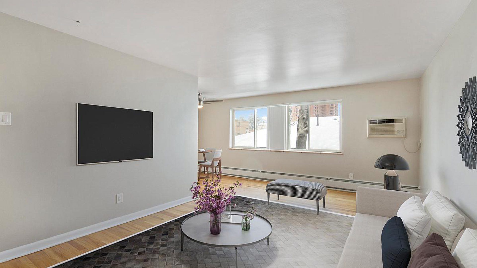 Living room with wood floor and tile, modern plush furniture, wall mounted TV, and large window.