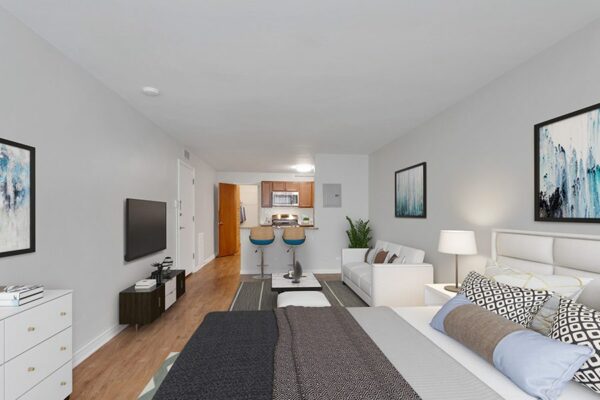 Studio living area with wood floor, plush bed, updated kitchen, and comfortable seating.