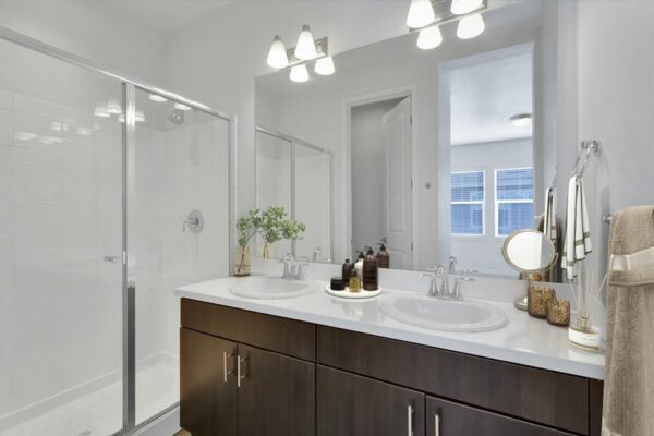 Rendering of a bathroom with his and hers sinks, shower, dark wood cabinets, and white countertops.
