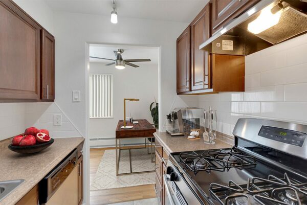 Apartment kitchen with wood floor and cabinets, stone counters, and stainless steel appliances.