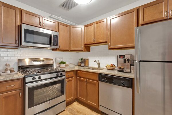 Apartment kitchen with wood floor and cabinets, stone counters, and stainless steel appliances.