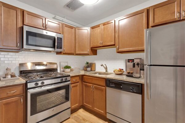 Kitchen with wood floor and cabinets, stone counters, stainless steel appliances, and tiled backsplash.