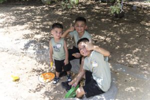three kids playing with toys and waving at camera